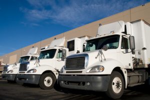 Three white long haul Semi trucks parked outside a shippping and receiving distribution warehouse.